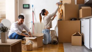 A man and a woman are packing boxes in a room, appearing to be in the process of moving