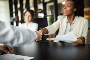 employer Employer-Paid Cancer Insurance vs Voluntary Cancer Insurance: What’s Best for Your Business This image shows two people shaking hands, with a third person blurred in the background, in a business meeting or agreement