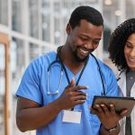 Two smiling healthcare professionals looking at and discussing something on a tablet computer