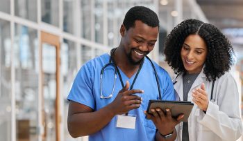 Two smiling healthcare professionals looking at and discussing something on a tablet computer