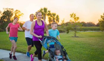 The image shows a family of five walking or running with a child in a stroller