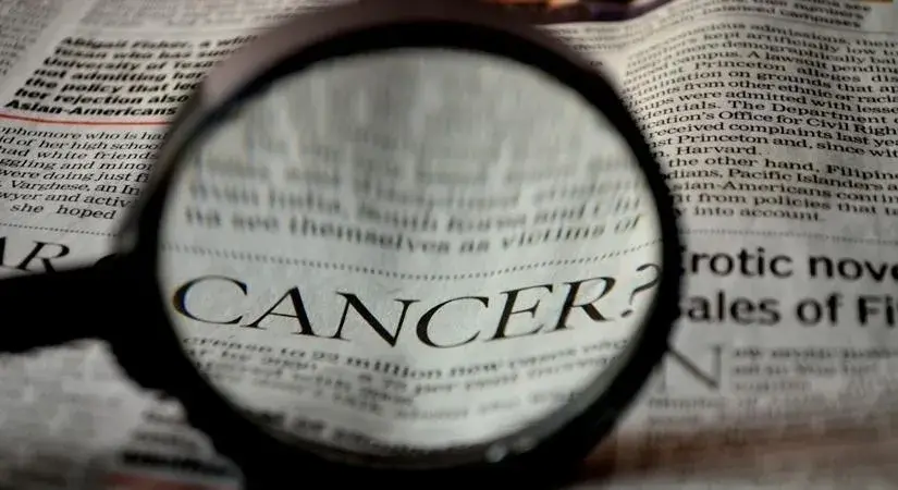 Cancer How Cancer Insurance Helps Employees During Treatment? A magnifying glass focussing on the word "CANCER" in a newspaper