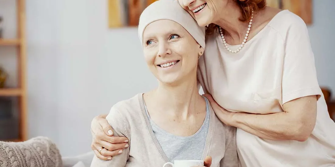 Critical Illness Insurance Two Woman Staying Positive and Sitting Together at Home Enjoying Their Time Together after a Successful Radiation Therapy Session Where to Find Critical Illness and Cancer Insurance for Your Business A smiling woman with a head covering, possibly undergoing cancer treatment