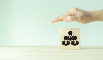 A hand hovering over a stack of blocks, arranged to depict three people in suits