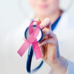 A doctor holding a stethescope with a ribbon that represents cancer