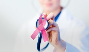 A doctor holding a stethescope with a ribbon that represents cancer